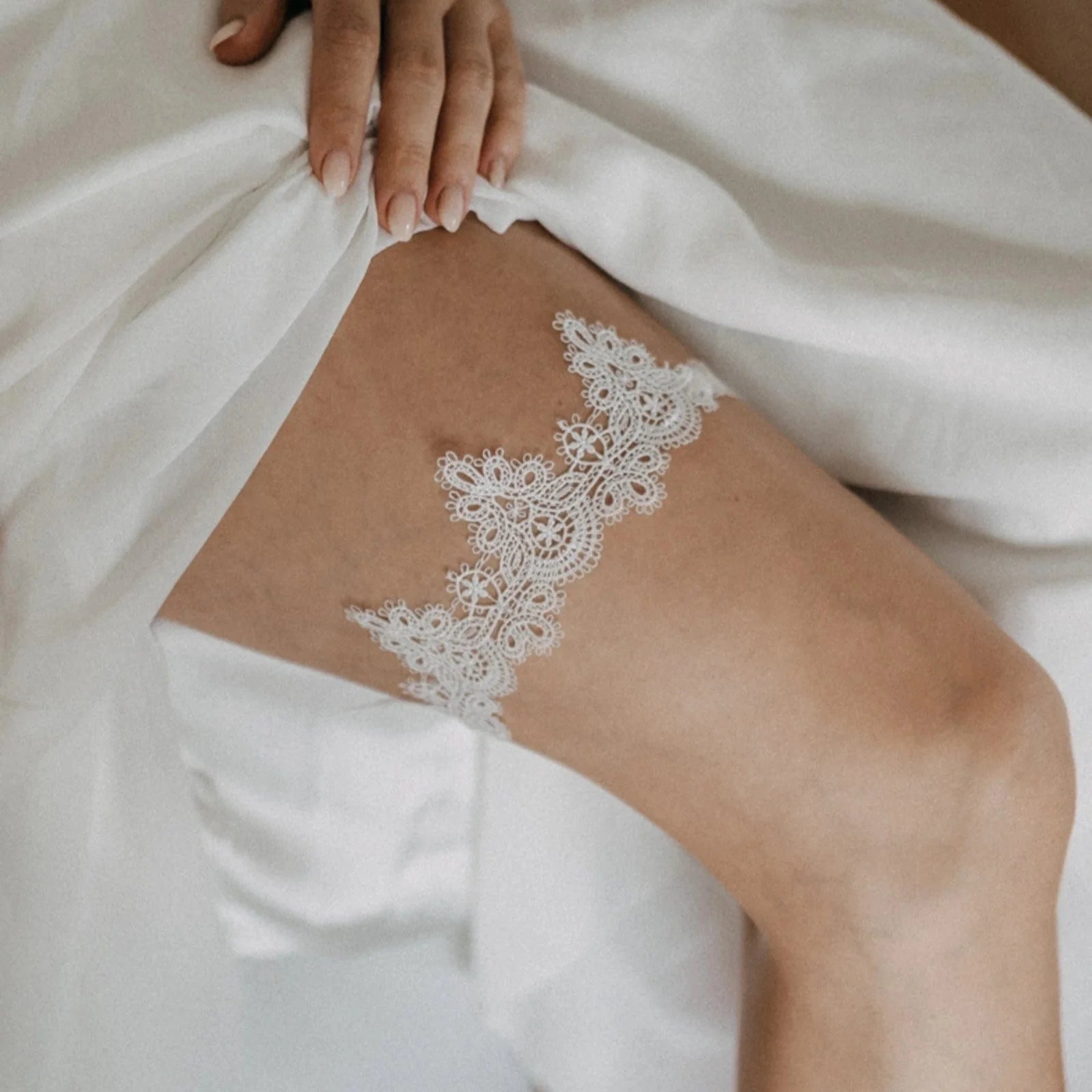 Ein zartes Strumpfband aus weißer Spitze mit einer kleinen Schleife aus blauem Band liegt auf einer rustikalen Holzfläche. Die Spitze ist mit einem floralen Muster versehen, und das Strumpfband ist ordentlich in einer horizontalen Position angeordnet.