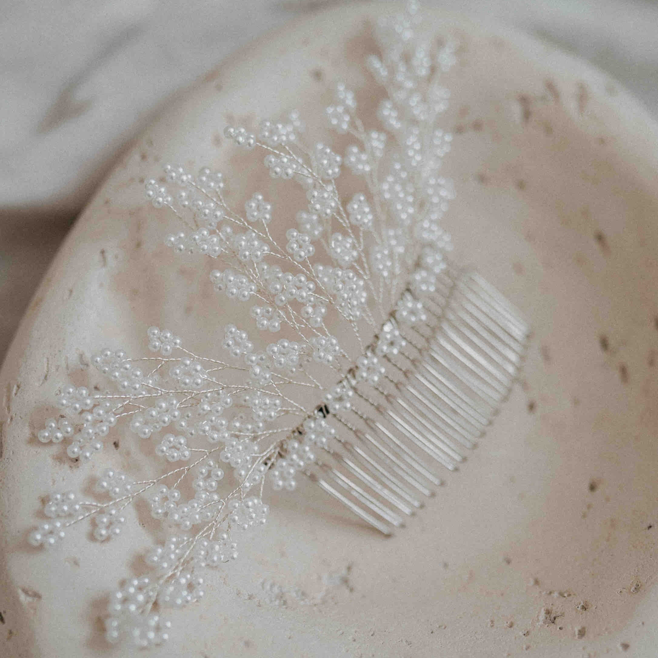 Die Haarkamm Braut mit Perlen (groß) von Fräulein Maya, verziert mit weißen Kunstperlen auf silbernen Drähten, eignet sich ideal als Hochzeit Kopfschmuck oder Vintage-Brautfrisur und liegt auf einer runden, strukturierten Keramikschale.
