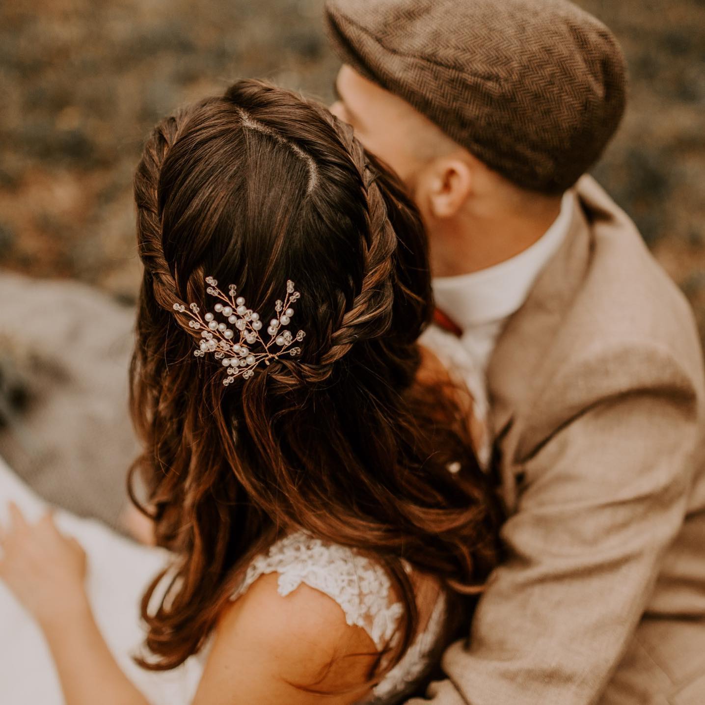 Eine Frau mit langen geflochtenen braunen Haaren, geschmückt mit Fräulein Mayas Braut Haarnadeln (2 Stück), sitzt im Freien neben einem Mann in einem hellbraunen Anzug und einer braunen Schiebermütze. Das Foto hebt ihren Hinterkopf und die eleganten Haarnadeln hervor.