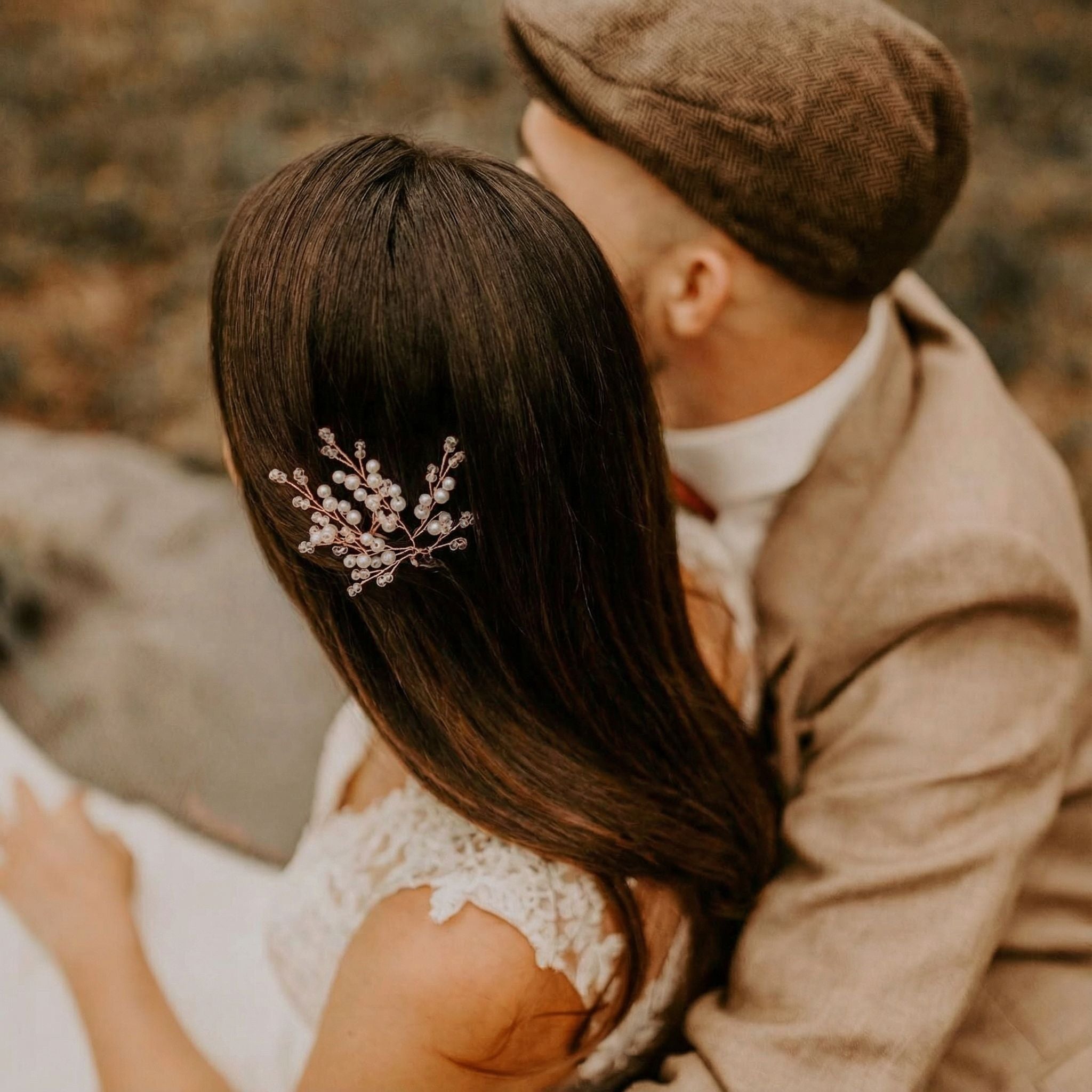 Eine Frau mit langem braunem Haar, geschmückt mit einer zierlichen Haarnadel aus Perlen und Kristallen, sitzt neben einem Mann mit brauner Schiebermütze und hellbraunem Anzug. Das Bild ist warm beleuchtet und weich fokussiert, so dass ein intimes Vintage-Gefühl entsteht. Ihre Gesichter sind teilweise abgewandt.