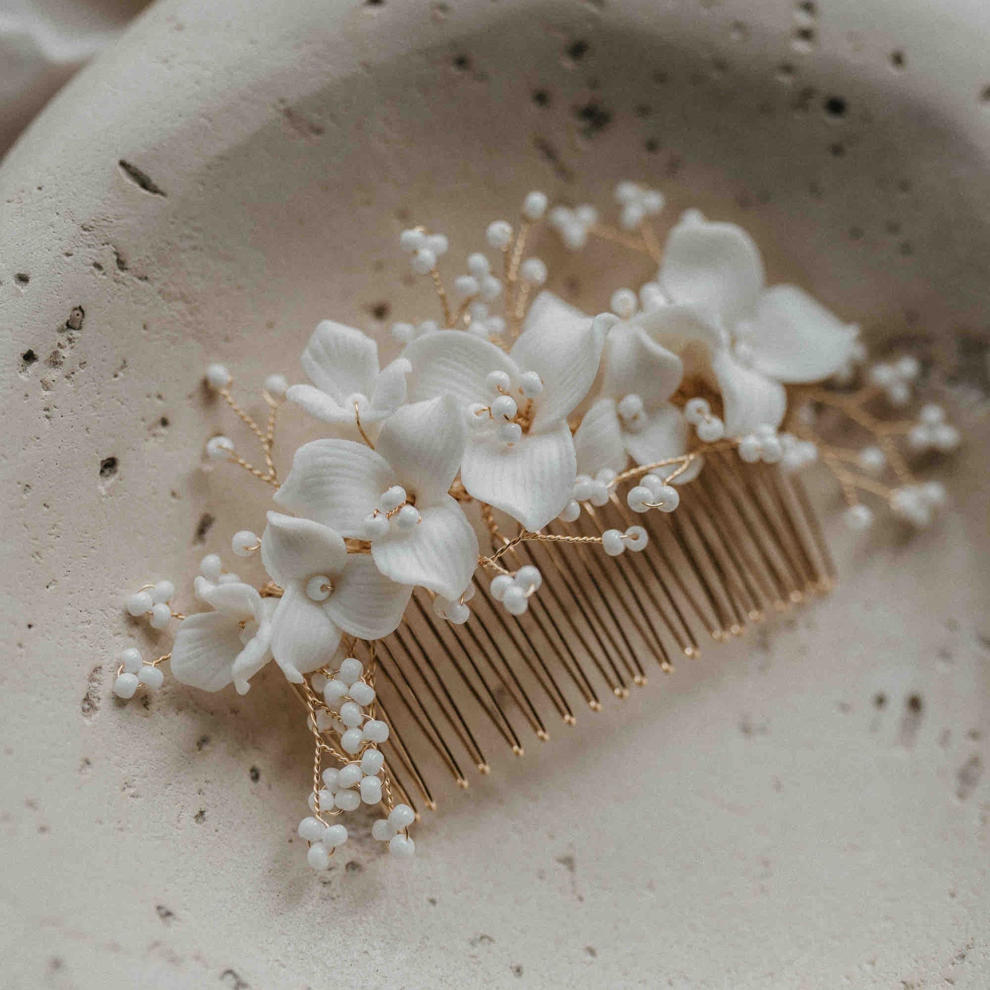 Der Keramik Haarkamm mit Blumen und Perlen von Fräulein Maya präsentiert zarte Blüten und perlenartige Akzente auf einer edlen, strukturierten Oberfläche - das perfekte Haar Accessoire für deine Brautfrisur.