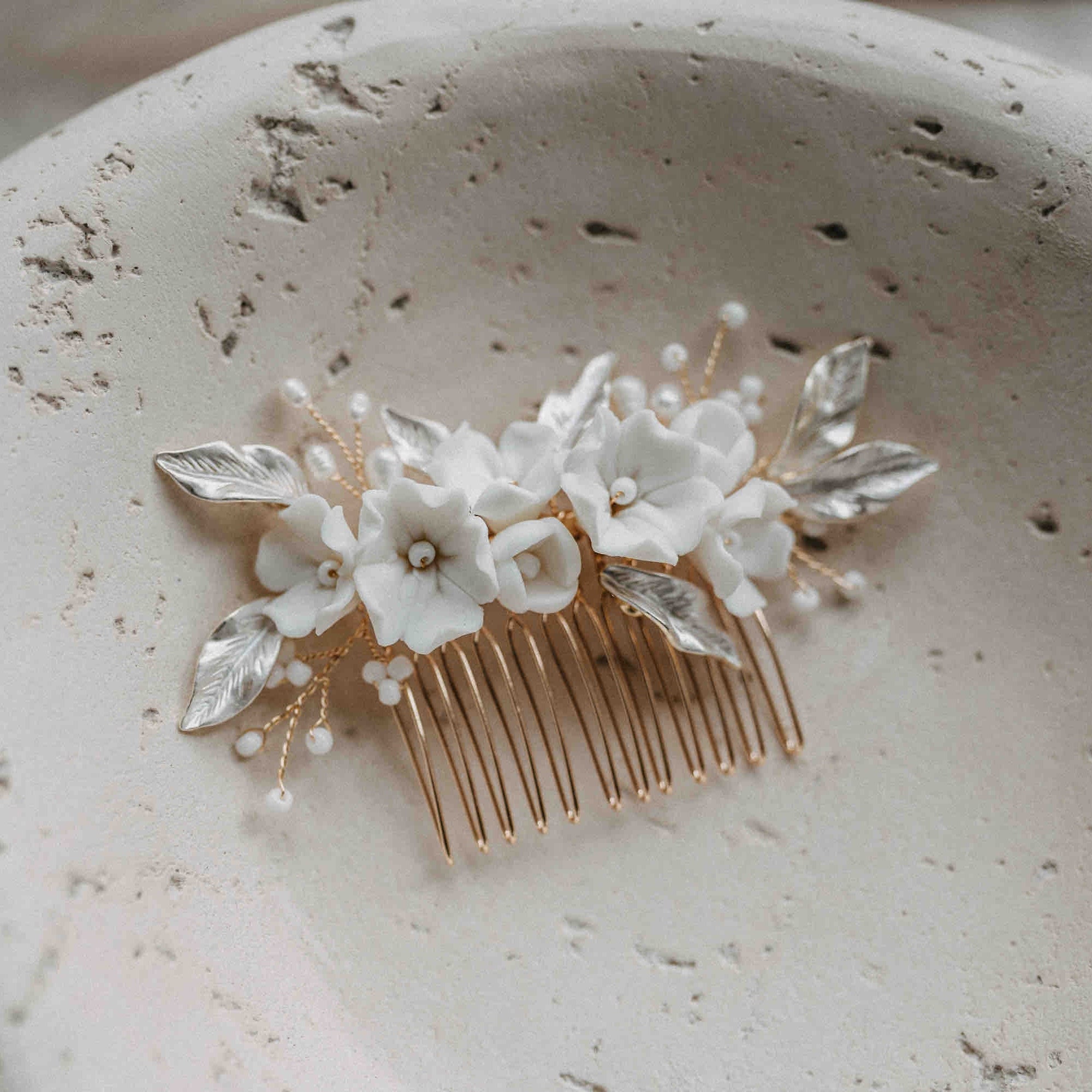 Der Haarkamm mit Keramik Blumen und Blätter von Fräulein Maya ist ideal als Haarschmuck Vintage oder Headpiece Brautfrisur. Mit weißen Keramikblumen, Perlen und Silberblättern liegt er in einer dezenten, marmorierten Schale.